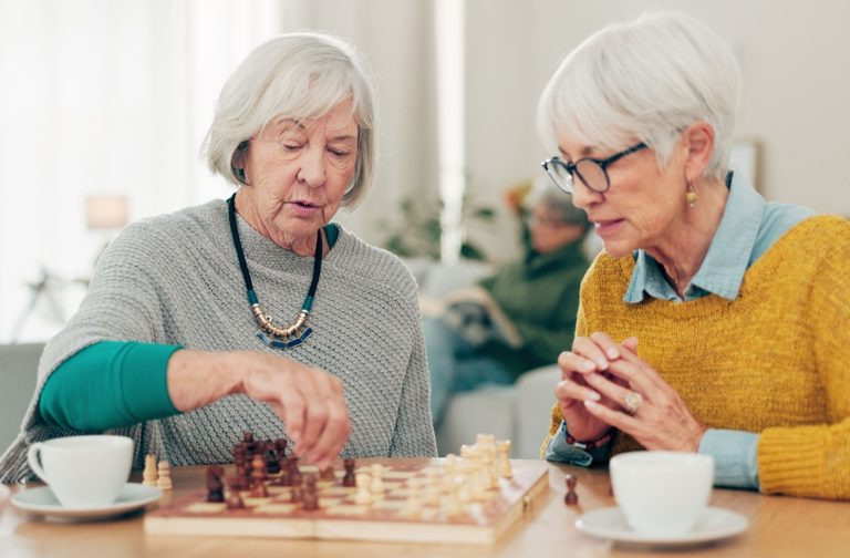 Two older women are playing chess for cognitive stimulation and social well-being.