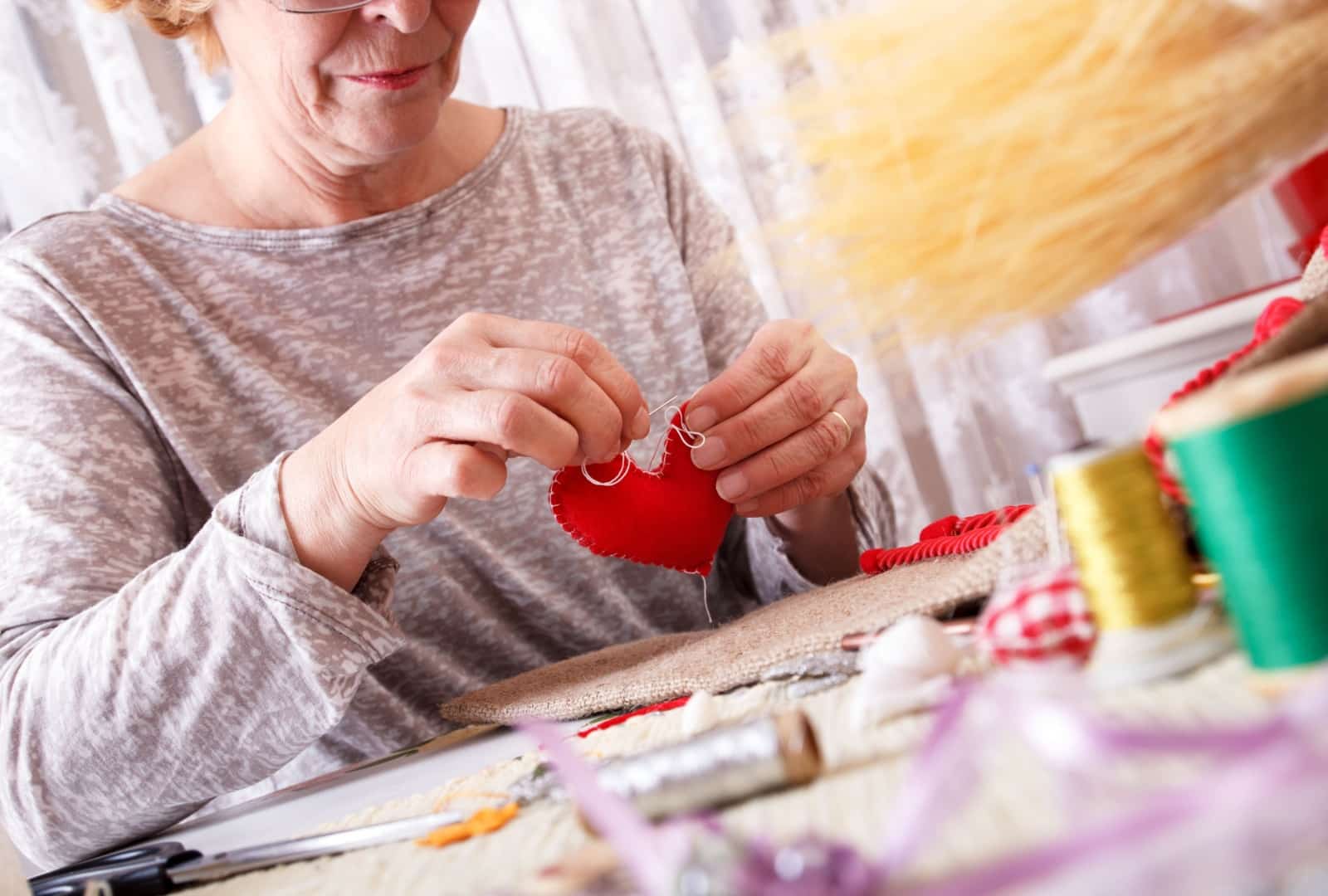 A senior woman sewing a red heart together and learning new sewing skills.