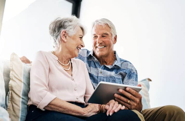 Happy elderly couple sharing a moment and looking at a tablet together, researching retirement communities.