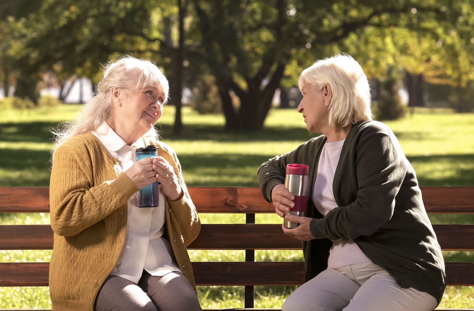 Two senior women chatting on a park bench, discussing their experiences in a retirement community.