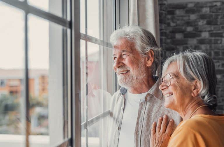 A happy senior couple smiling while looking out the window of a luxury senior living community.