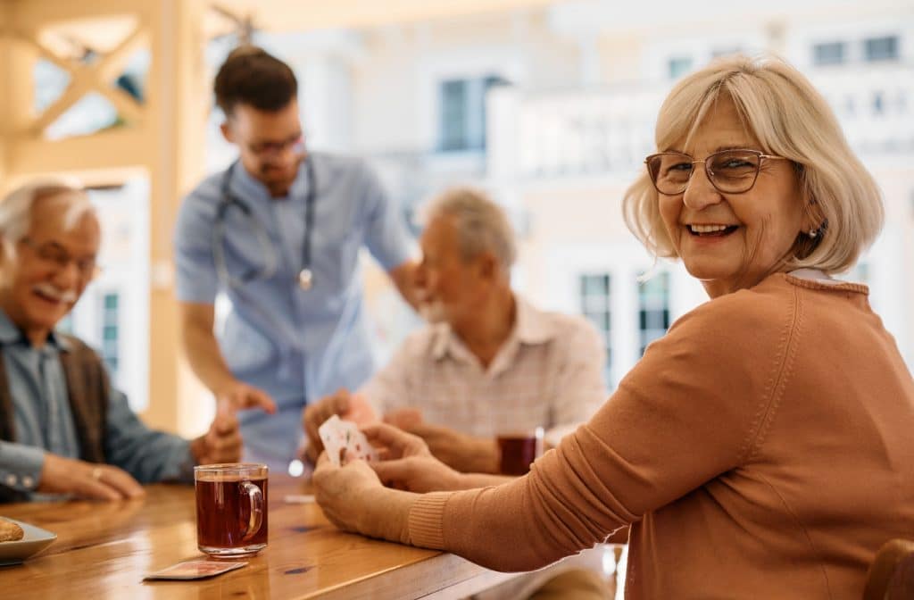 A group of seniors laughing while playing cards on the patio in a luxury senior living community.
