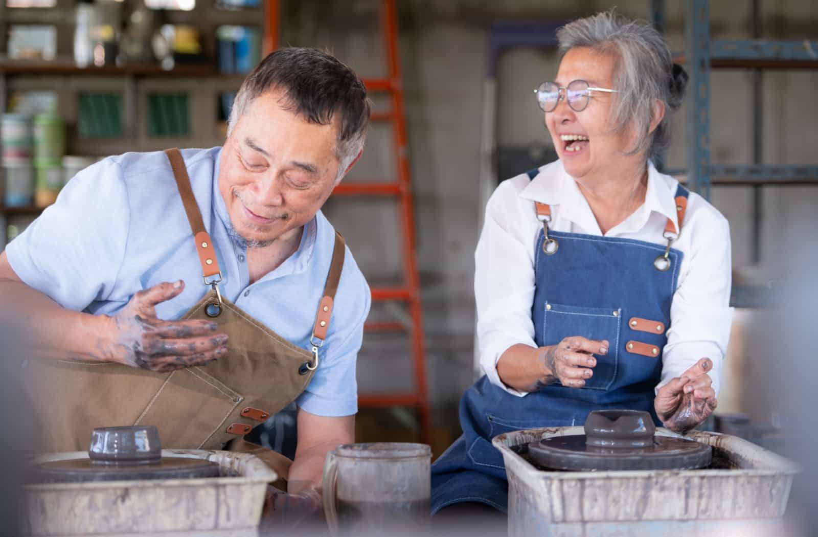 A senior man and woman making friends and laughing together at a pottery workshop.