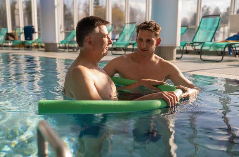 An older man is engaging in aquatic therapy with a certified aquatic therapist.