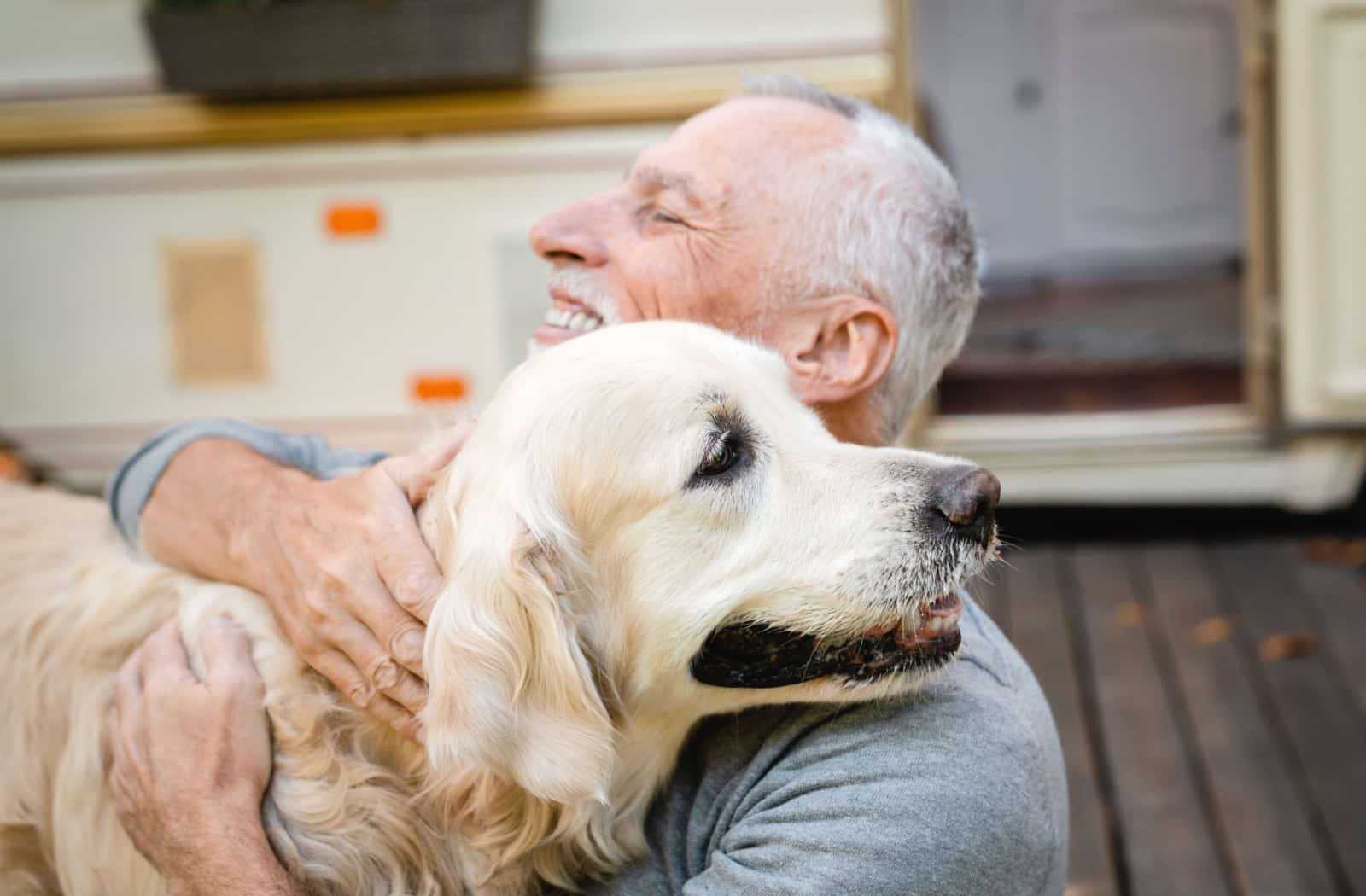 A cheerful senior hugs a golden retriever therapy dog.