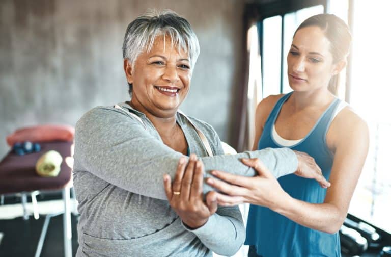 A personal trainer guides a senior through gentle stretches to help improve her mobility and flexibility.