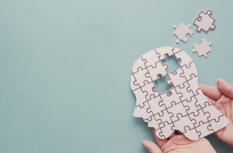 A person holding a puzzle of a side profile of a person with a few puzzle pieces missing symbolizing dementia.