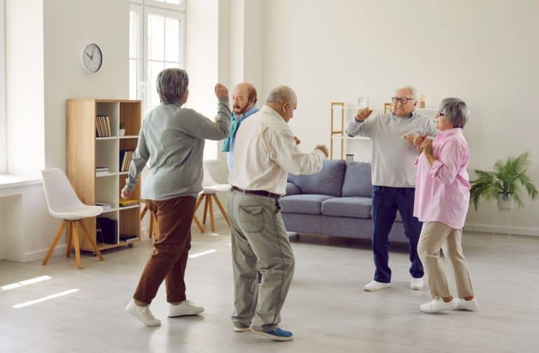 A group of happy seniors are dancing enthusiastically in an open room during a senior dance class.