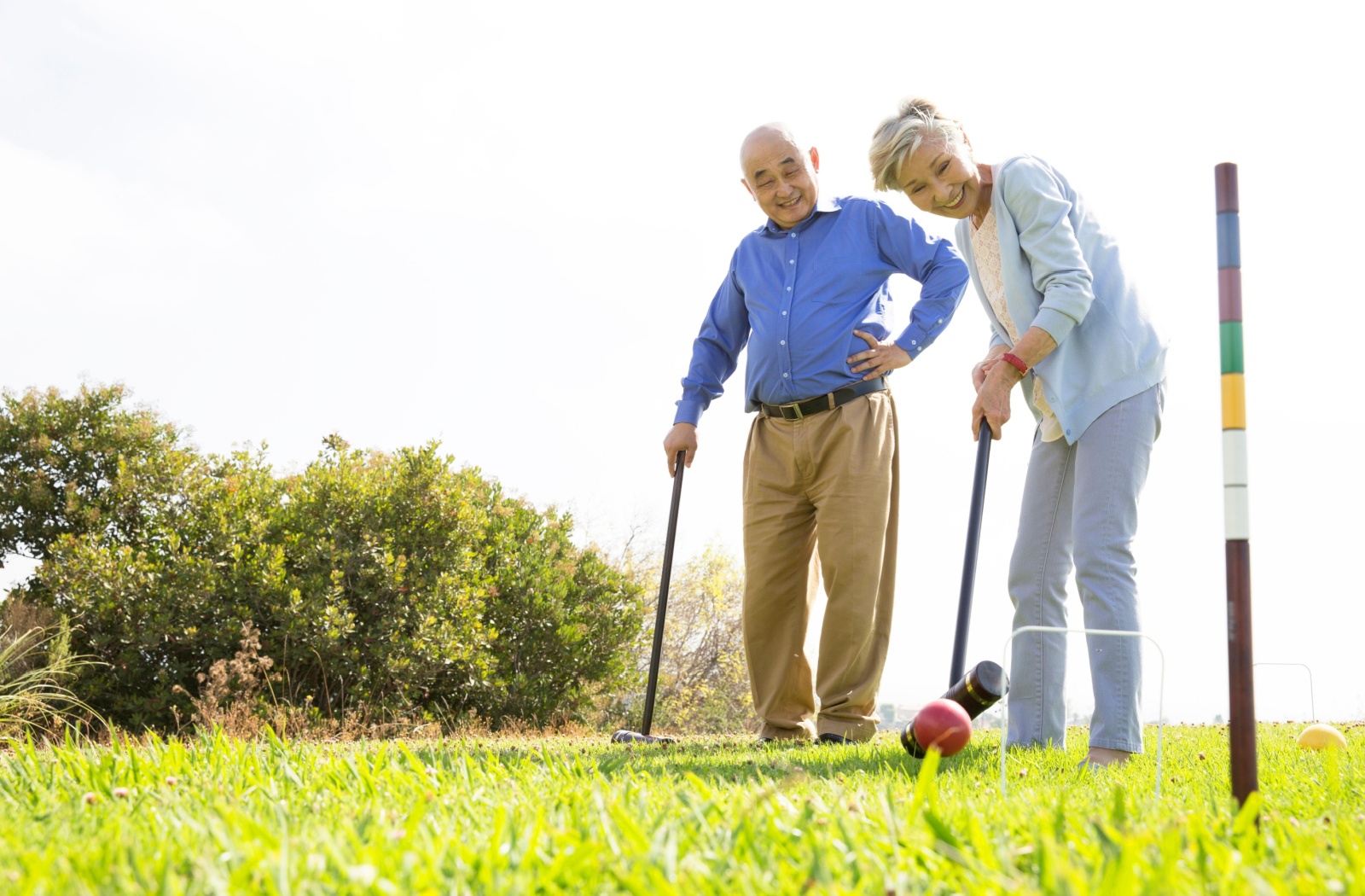 A senior couple plays croquet on an outdoor lawn.