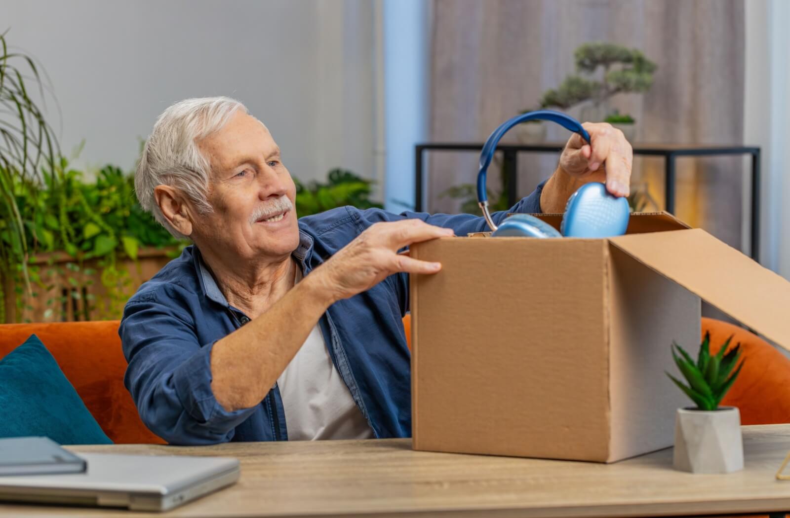 A happy senior pulls a new set of headphones out of a gift box to enjoy their audiobooks and TV shows.
