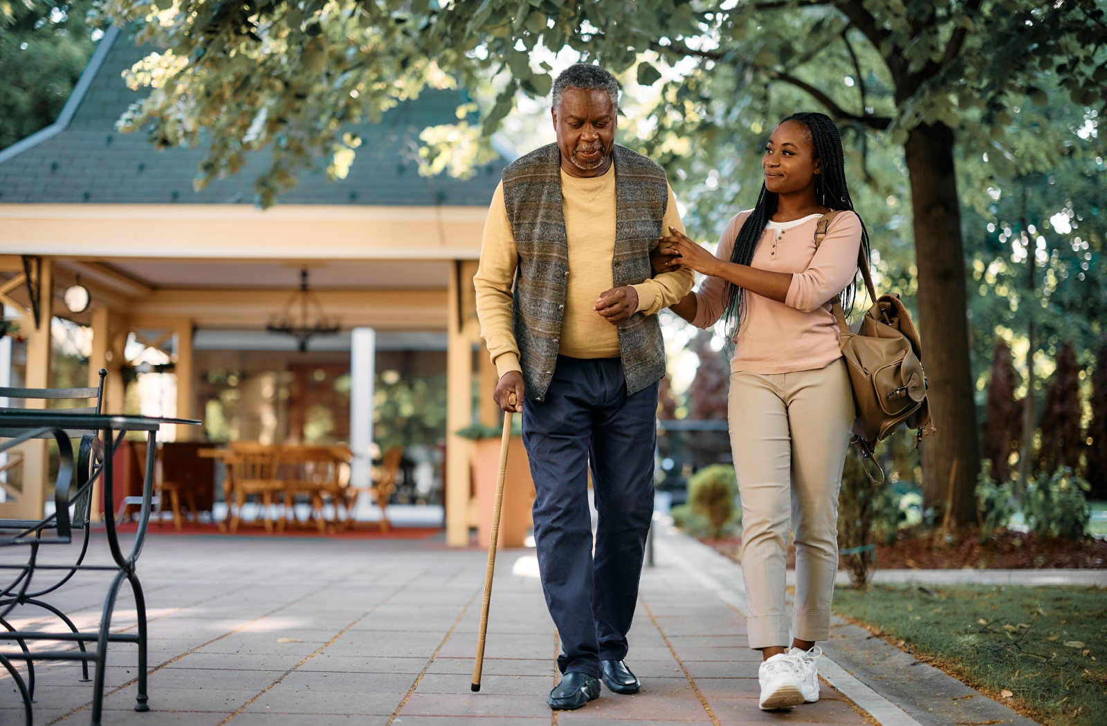 A senior resident walks with a cane and their teen grandchild through the community garden.