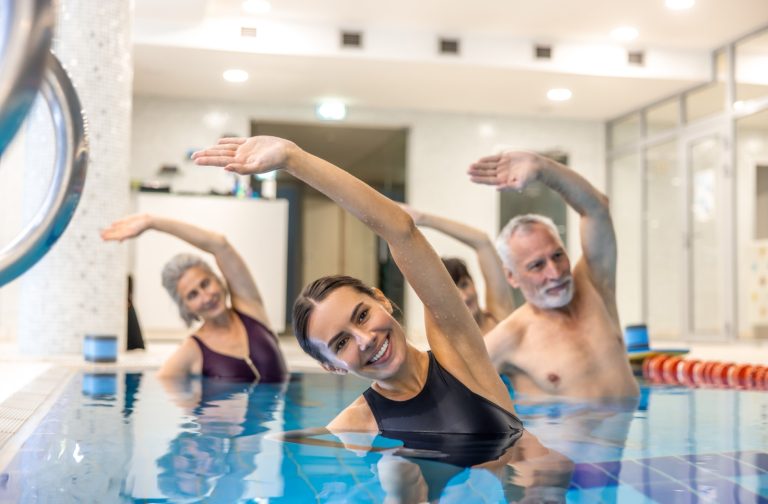 An image of seniors in a swimming pool with an instructor enjoying some swimming pool exercises together.