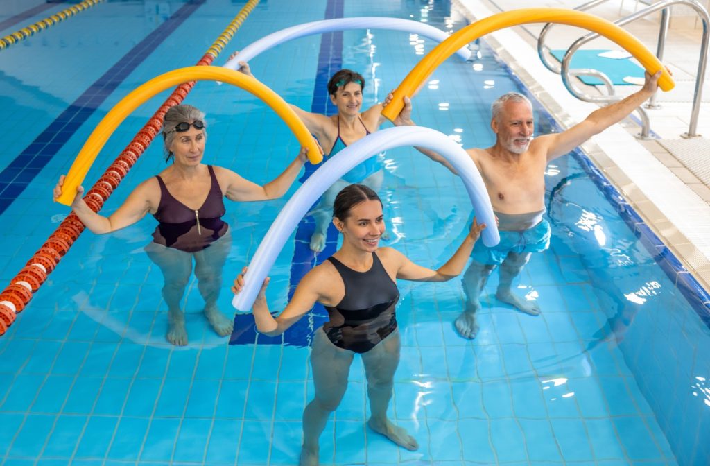 A group of happy seniors in a swimming pool exercising together with their instructor
