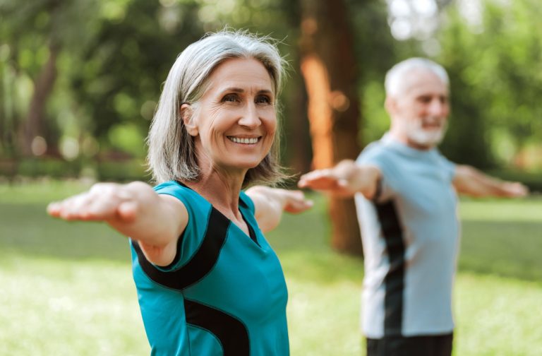 A senior couple happily stretching and being active in the park to reduce the signs of aging.