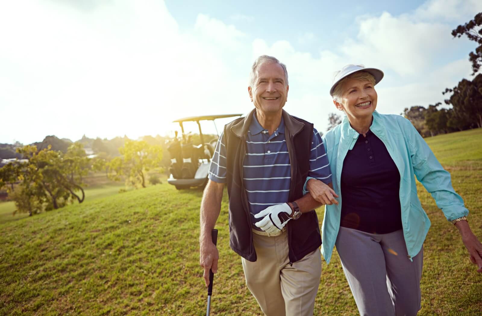 Smiling senior couple walking on a golf course, showcasing how outdoor activities promote happiness and healthy living.