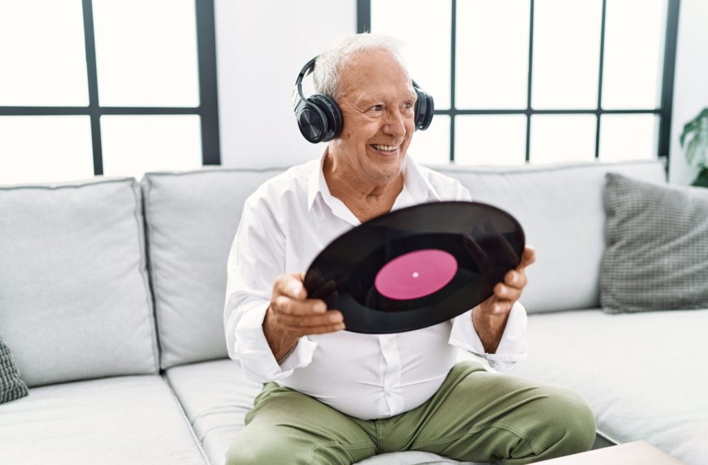 A happy senior holding up a vinyl record while listening to music with their headphones on.