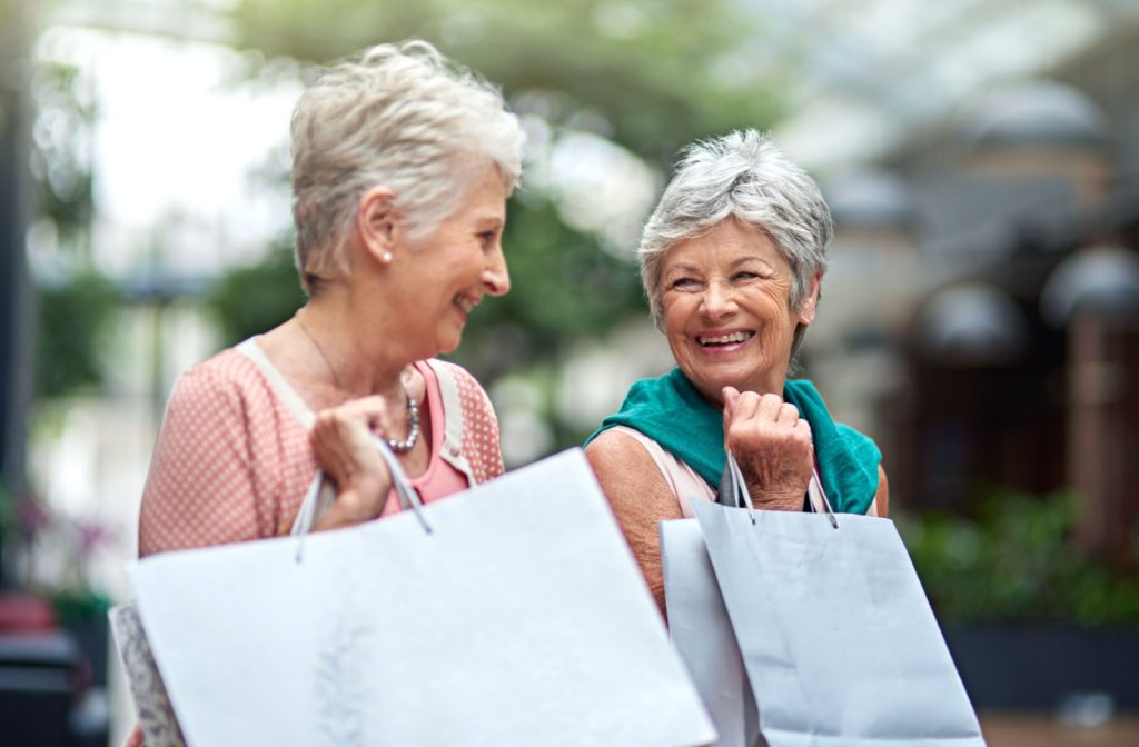 Two older adults smiling at each other while carrying shopping bags from a shopping trip at Toco Hills.