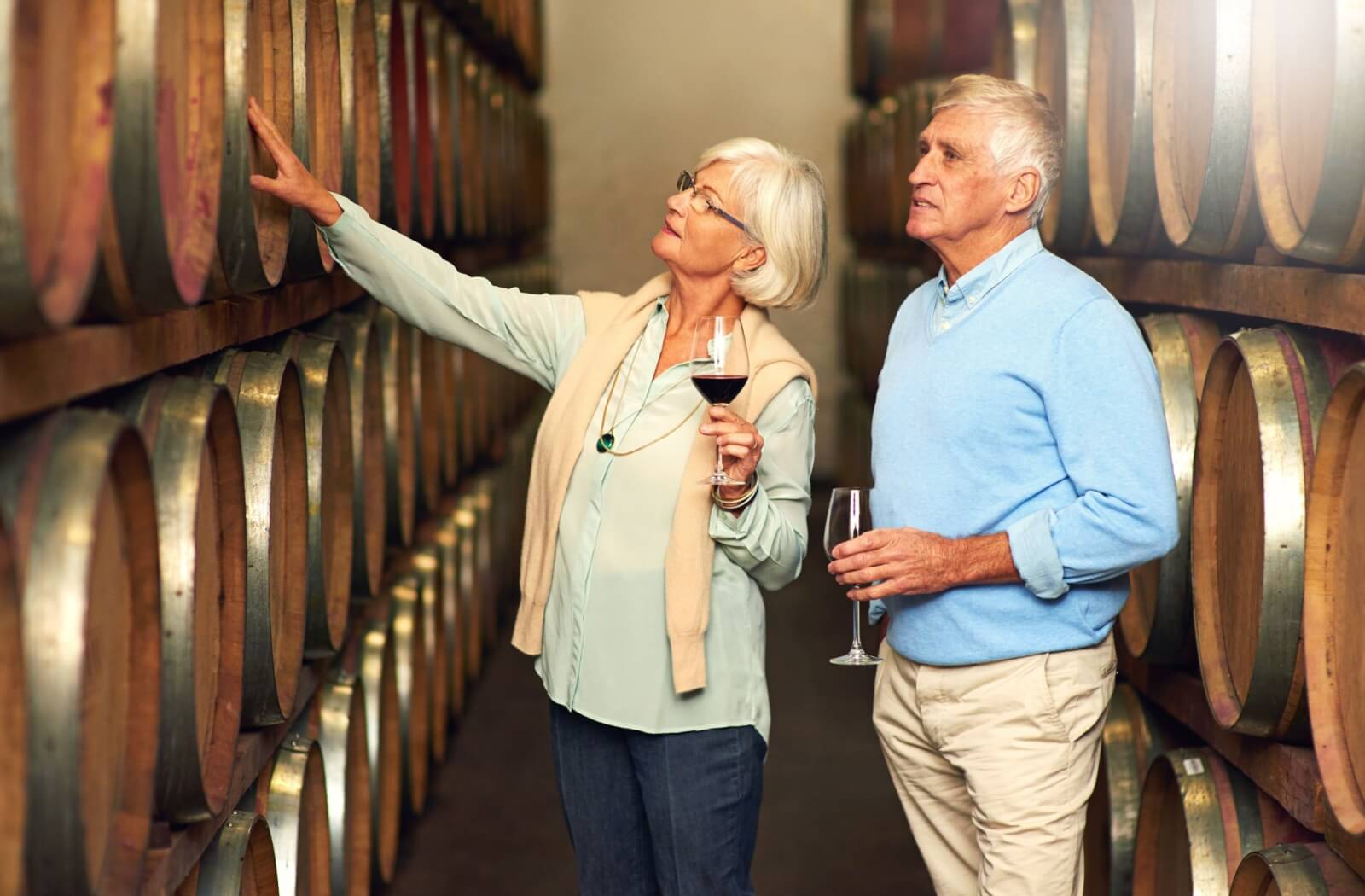 An older couple tour a winery while drinking some samples.