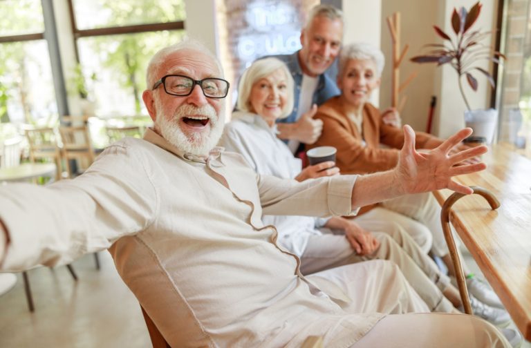 A mature adult enthusiastically smiling in the camera while enjoying quality time with friends.