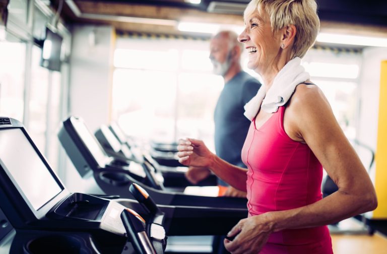 An older adult running along a row of treadmills during a cardio fitness class.