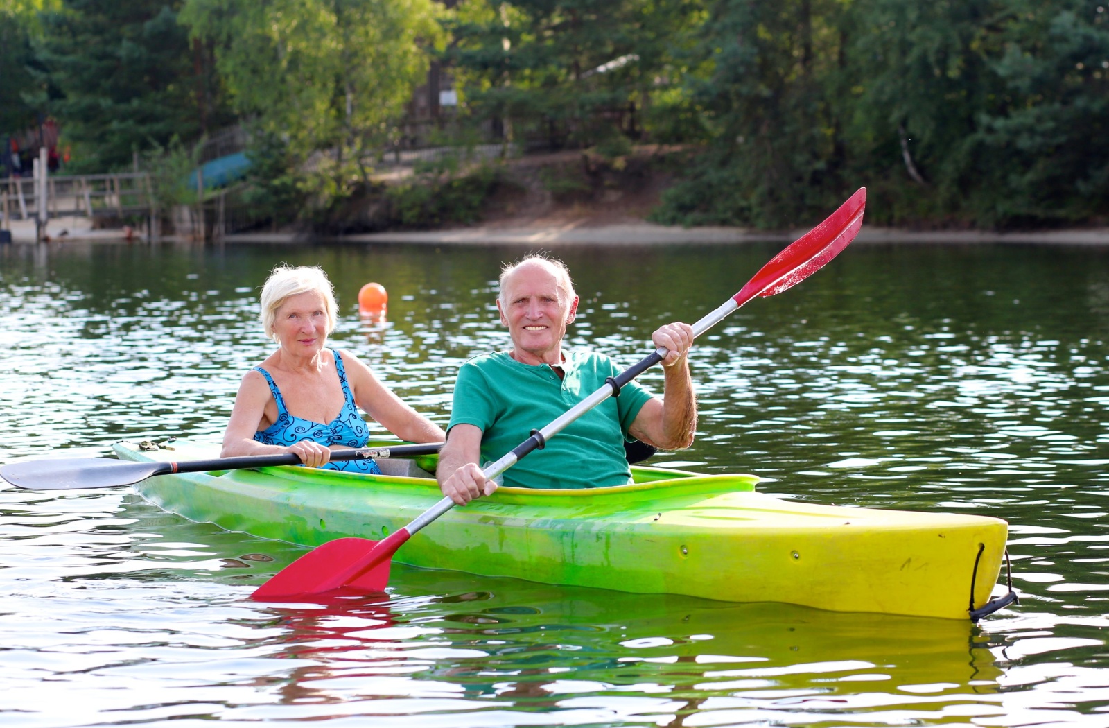 Two older adults kayaking on a calm lake surrounded by trees enjoying outdoor exercise and nature connection
