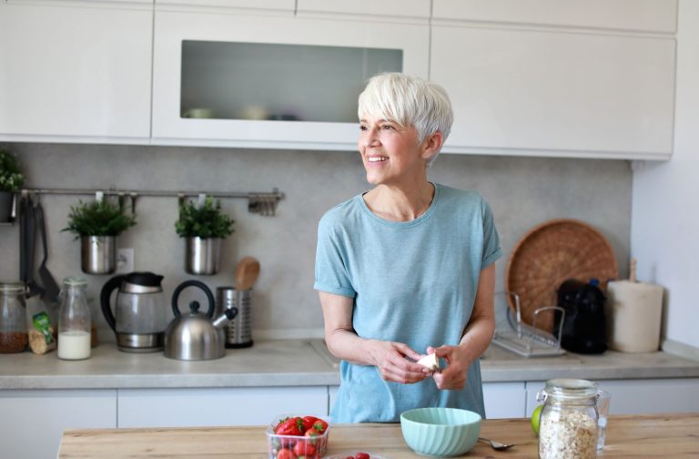 Older adult preparing a healthy snack in a bright kitchen with yogurt fruit and oats on the counter