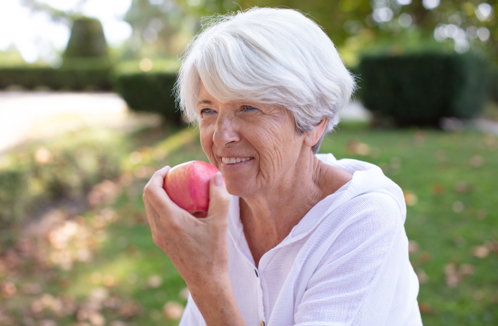 Older adult enjoying a fresh apple outside in a garden setting promoting healthy snacking and senior nutrition in nature
