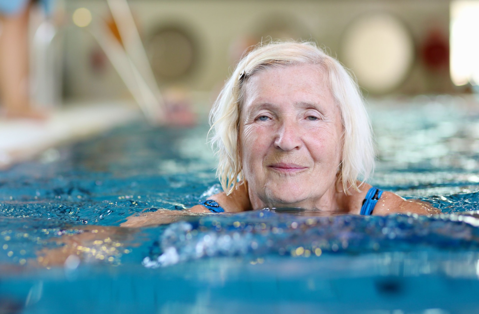 An older adult smiles while swimming in the pool in their senior living community
