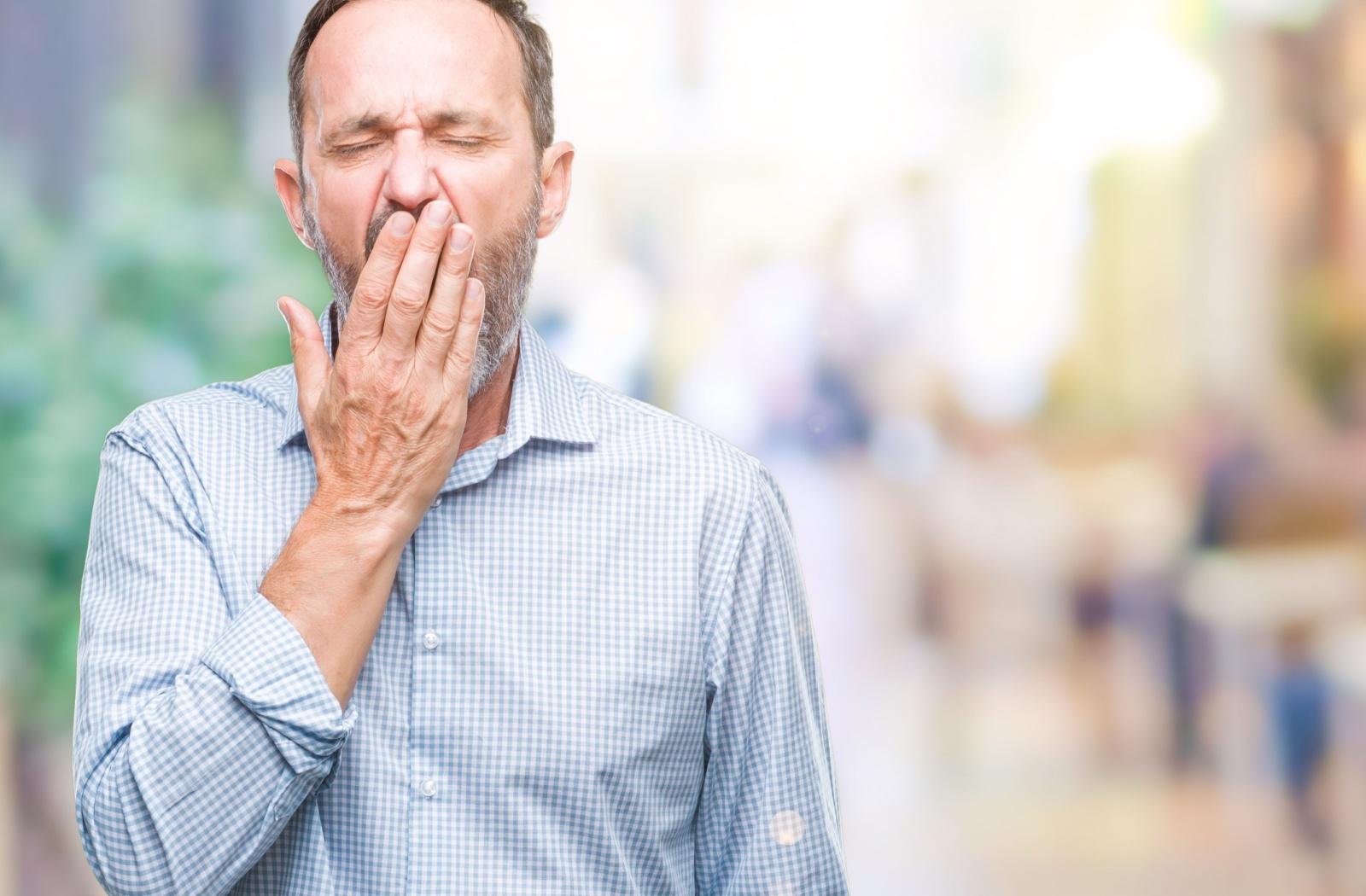 A senior yawns, covering their mouth with their hand, from a restless night.
