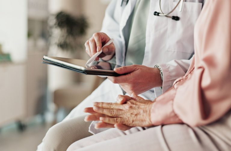 A doctor taps a tablet screen with a pen after a checkup to show an older adult the results of their dementia diagnosis