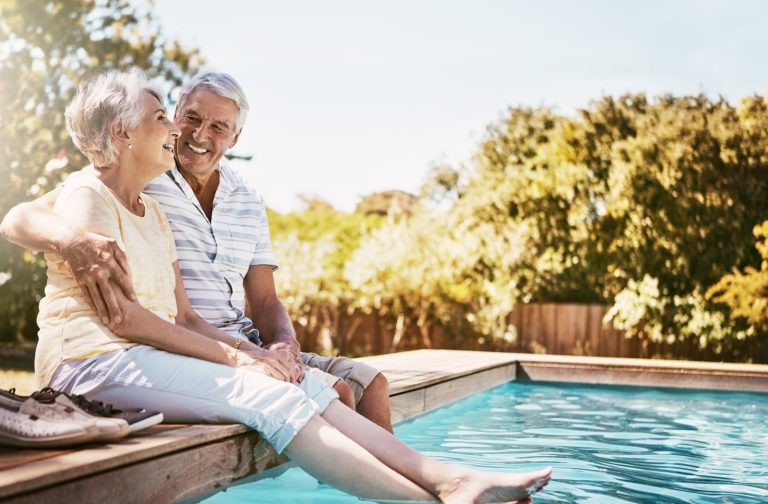Two seniors dip their feet in an outdoor pool on a hot summer day