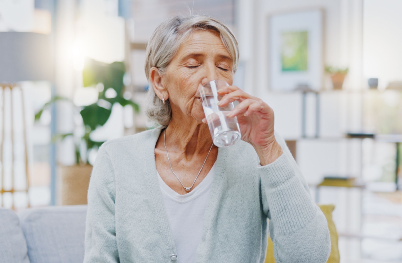 A senior sips on a glass of water inside their apartment, taking a break from the outdoor heat.